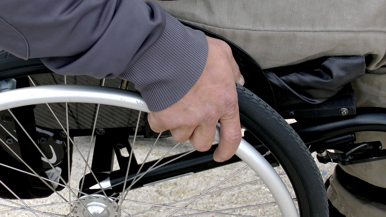 Foto da mão de uma pessoa segurando o aro de impulsão de uma cadeira de rodas. 