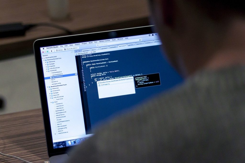 Foto de uma pessoa na frente de um laptop que mostra diversos códigos na tela. 