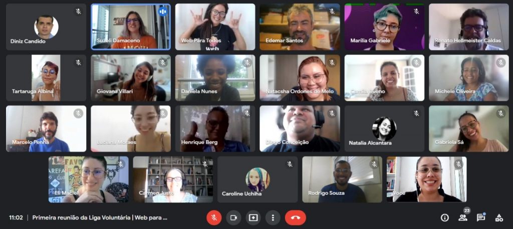 Print da tela de uma reunião virtual com 23 pessoas diversas em janelas distintas de chamadas em vídeo. A maioria sorri