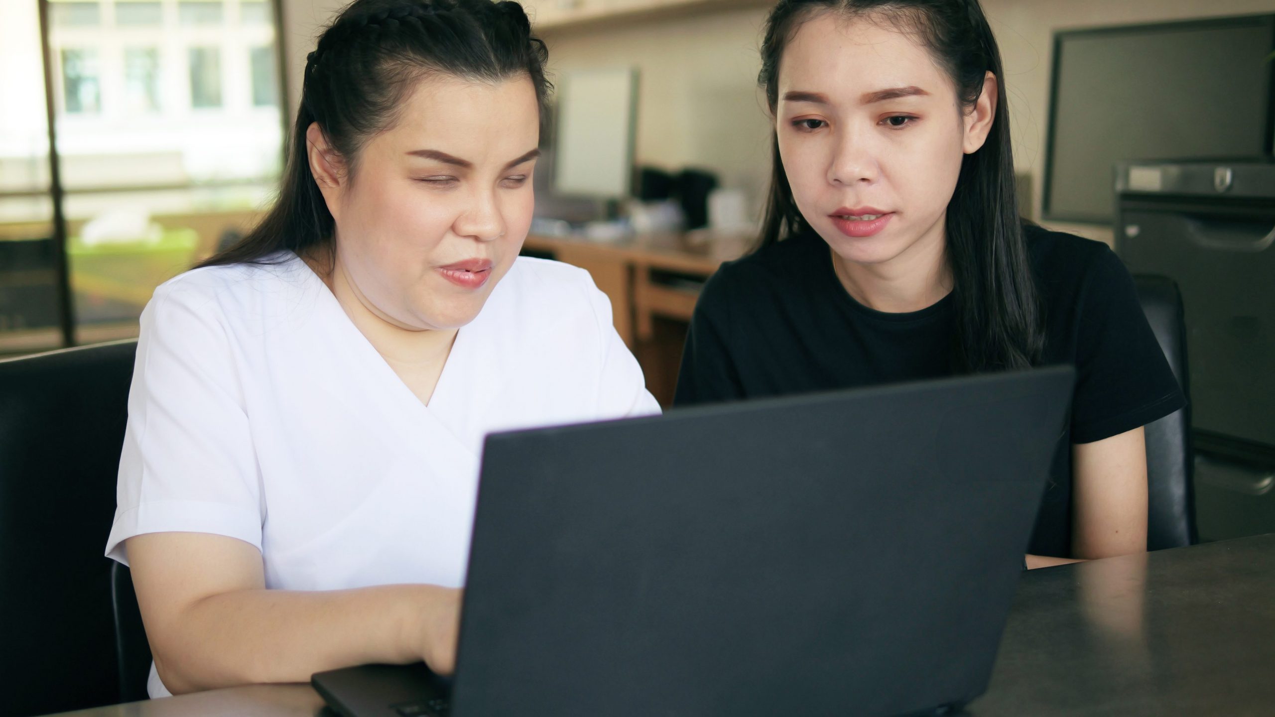 Foto de duas mulheres em frente a um notebook. Uma delas é cega e está com suas mãos apoiadas no teclado como se estivesse digitando.