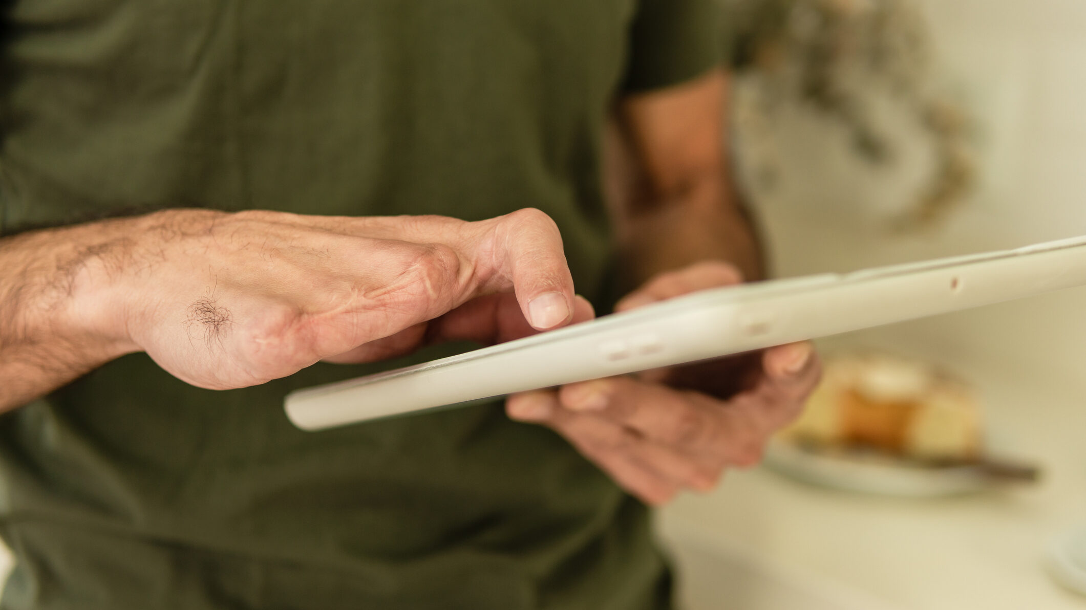 Foto em close de mãos masculinas segurando um tablet. Uma delas tem três dedos amputados.