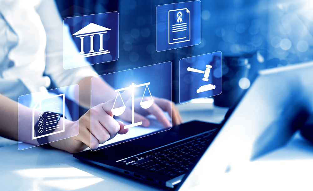 Mãos de uma pessoa no teclado de um laptop enquanto toca o ícone digital de uma balança da justiça. Ao redor flutuam outros símbolos jurídicos iluminados em tom azul.