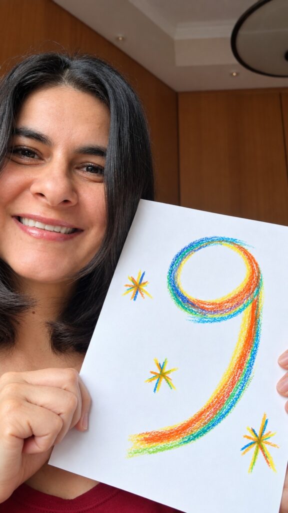 Claudia Nascimento sorri enquanto segura, com as mãos, uma folha de papel com o número 9 e um asteriscos desenhados.
