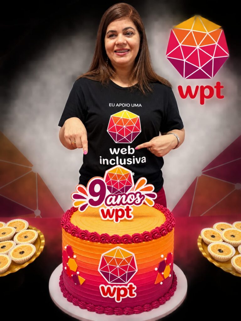 Doriane Vasconcelos sorri em pé diante de uma mesa com um bolo decorado nas cores do Web para Todos e um enfeite com a frase '9 anos WPT'. Ela veste camiseta preta com o texto 'Eu apoio uma web mais inclusiva' e a marca do WPT, que também é exibida à sua esquerda.
