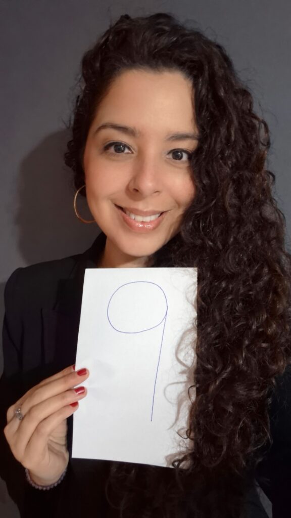 Elza Maria Albuquerque sorri enquanto segura, com a mão direita, uma folha de papel com o número 9 desenhado.