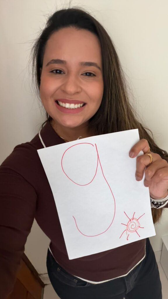 Gabriela Sá sorri enquanto segura, com a mão esquerda, uma folha de papel com o número 9 e um sol desenhados.