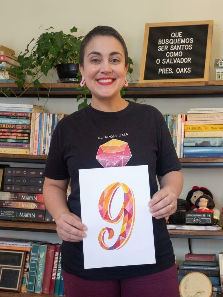 Natália Alcantara sorri enquanto segura, com as duas mãos, uma folha de papel com o número 9 desenhado nas cores do logotipo do WPT.
