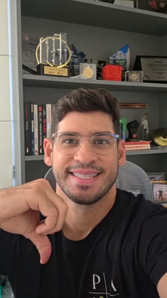 Ronaldo Tenório sorri enquanto faz o sinal do número 9 em Libras com a mão direita.
