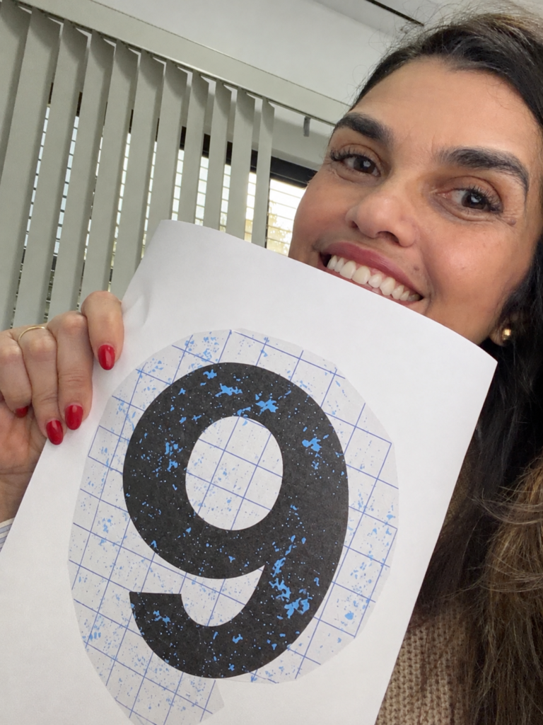 Taiane Fernandes sorri enquanto segura com a mão direita uma folha com o número 9 impresso.